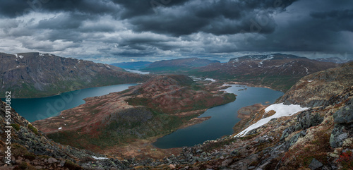 Turquoise and blue lakes in mountain landscape from above the hike to Knutshoe summit in Jotunheimen National Park in Norway, mountains of Besseggen in background, dark cloudy sky, moss in foreground