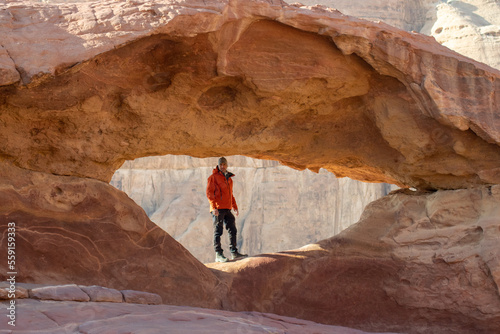 person on a rock, under an arch, wadi rum, jordan