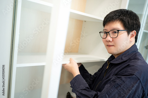 Home renovation or House remodeling concept. Asian male furniture assembler or Interior construction worker man installing white shelf panel in the cabinet. Furniture installation for the new house.