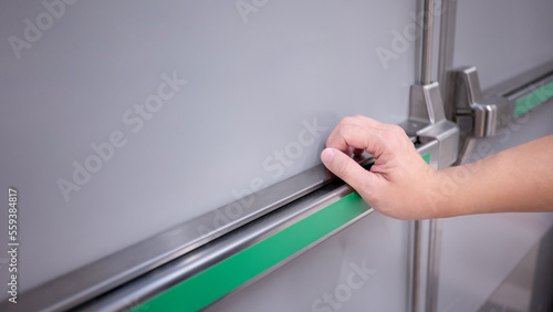 Male hand pushing stainless steel panic bar opening the emergency fire exit door in public building. Fire escape concept