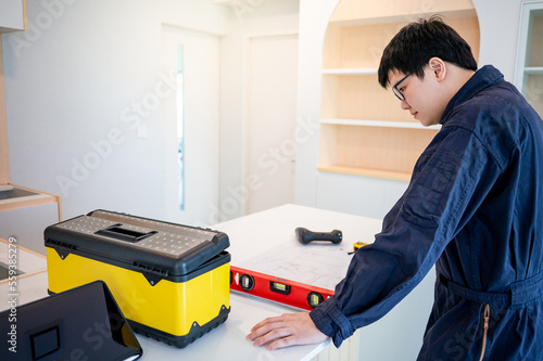Home renovation or house remodeling concept. Asian male interior manual worker working with construction tools on countertop of new kitchen. Furniture assembler man installing cabinet and counter.