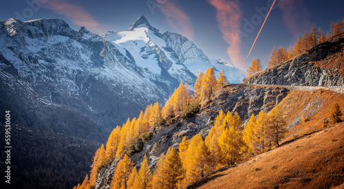 Incredible autumn landscape during sunset. Scenic view on mountain highland with colorful trees and perfect blue sky in the background the beautiful Grossglockner. Amazing nature background. postcard