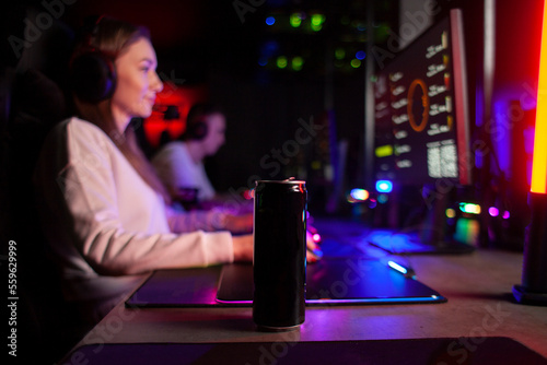 girl gamer sits at a computer and drinks an energy drink, a woman plays in a computer club at night and holds a drink