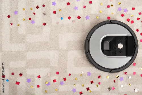 Modern robotic vacuum cleaner removing confetti from carpet, top view. Space for text