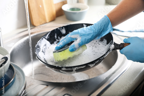 Woman washing dirty frying pan in sink indoors, closeup