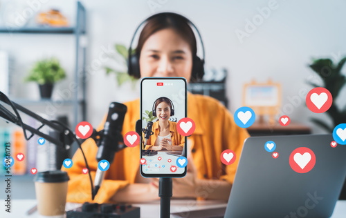 Vlogger live streaming podcast review on social media, Young Asian woman use microphones wear headphones with laptop record video. Content creator concept.