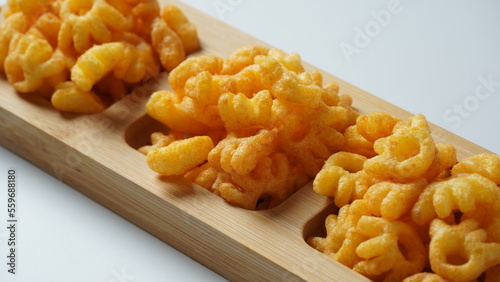Cheetos is a crunchy corn puff snack. Bright orange cheese puffs in a wooden board.