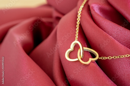 A gold necklace with a gold heart-shaped pendant resting on a pinkish-red fabric is the perfect gift for love, anniversary or special occasions on Valentine's Day.