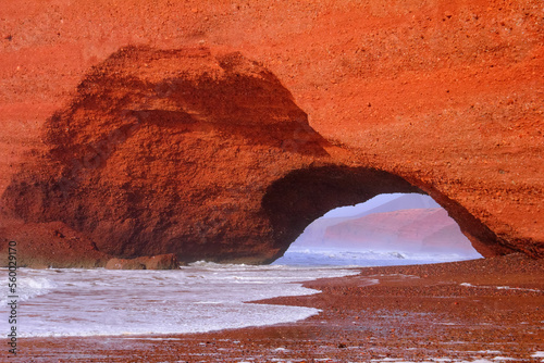 Legzira (Lazgira) beach, Morocco, Northwest Africa. Beautiful nature view, famous red mountain arch, pathway, foggy rocks, stormy Atlantic ocean, pebble coast and white foam of sea surf.