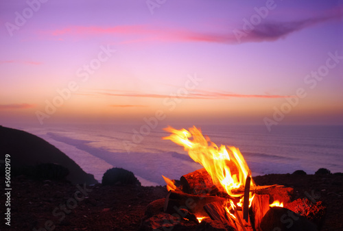 Sunset time in Legzira beach, Sidi Ifni, Morocco, Africa. Beautiful nature view, bonfire is burning on a high shore of Atlantic ocean, dark earth and sea surf at the background of colorful evening sky