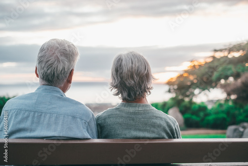 Head shot close up portrait happy grey haired middle aged woman with older husband, enjoying sitting on bench at park. Bonding loving old family couple embracing, looking sunset..