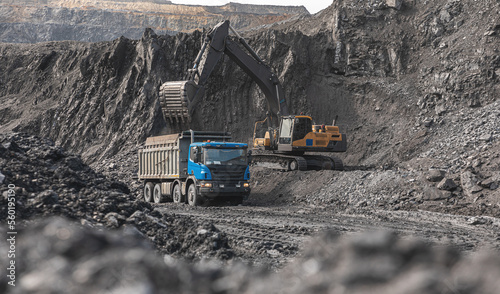 Large quarry dump truck. Big yellow mining truck at work site. Loading coal into body truck. Production useful minerals. Mining truck mining machinery to transport coal from open-pit production