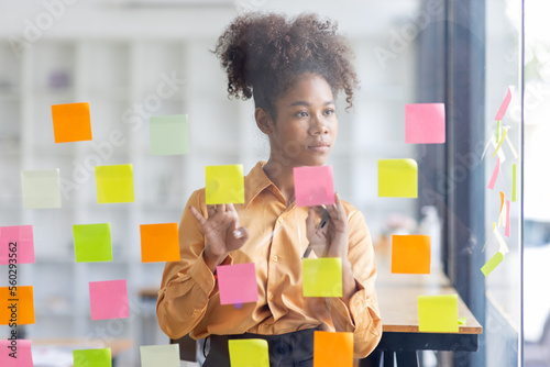 Young Serious african american Creative team use post it notes to share idea sticky note on glass wall. Asian business people design planning and Brainstorming thinking sticky History notes concept.