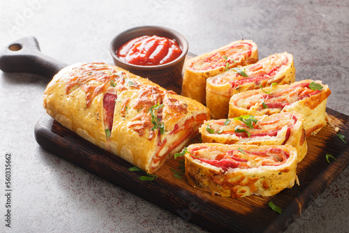 Italian stromboli, delicious pizza roll filled with sausage and ham closeup on the wooden board on the table. Horizontal