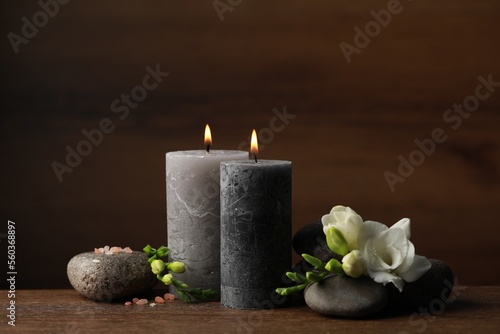Beautiful composition with burning candles, spa stones and flowers on wooden table
