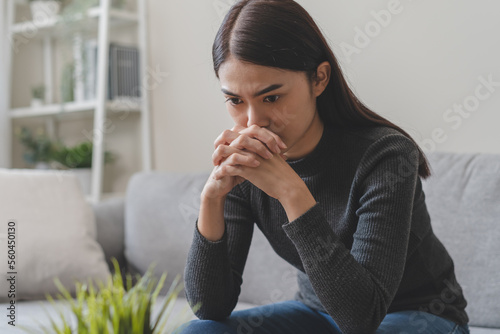 Unhappy anxiety young Asian woman sitting on the sofa at home.