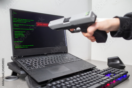 Człowiek celujący z broni do laptopa. Laptop wyświetlający napis ACCESS DENIED. Laptop wyświetlający komunikat BRAK DOSTĘPU. Hacker celuje z broni. Celowanie z pistoletu. Hacker aims with a gun.
