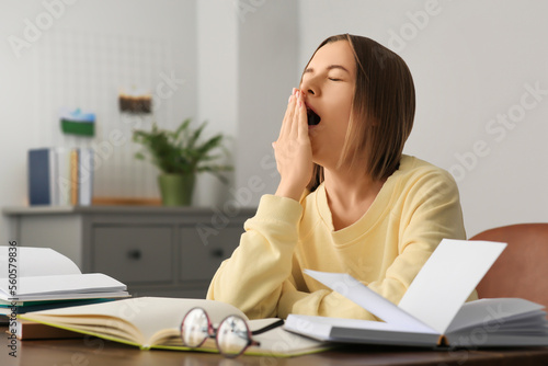 Young tired woman studying at wooden table in room