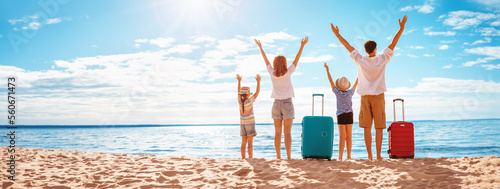 Mother and father with their children standing on the beach with suitcases.