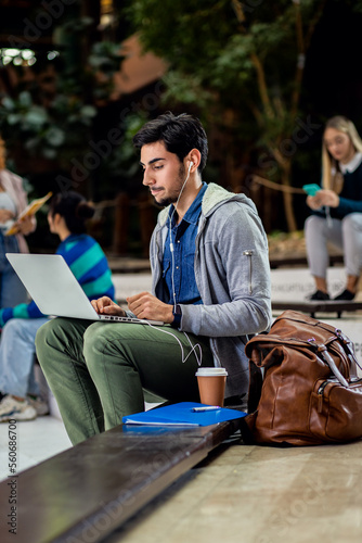 Portrait of male student siting in campus using laptop.