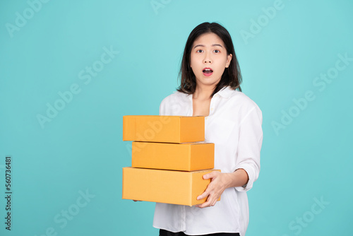 Young beautiful Asian businesswoman in white casual dress standing isolated on light green background. She is shocked and holding package parcel box.