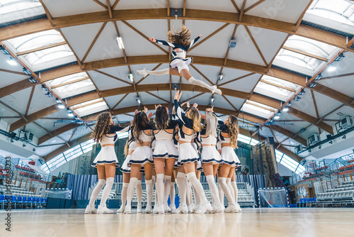 A group of cheerleaders are captured in a dynamic and athletic moment, performing a stunt by lifting one of their team members into the air. Showcasing energy, athleticism and unity in cheerleading.