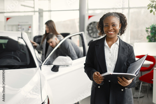 Black saleswoman standing at auto showroom and looking at camera