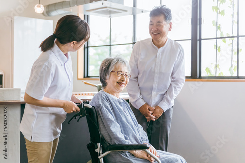 車椅子に座る高齢者夫婦と介護士・理学療法士・介護スタッフの女性 