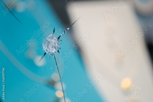 Detail of pierced hole in broken and shattered shop window of jeweler after attempted theft with blurred jewelry in background on display