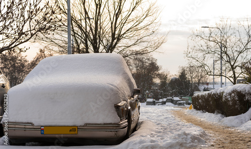 Zabytkowy amerykański samochód ( " krążownik szos" ) pod obfitą warstwą śniegu , zaparkowany na parkingu polskiego osiedla .