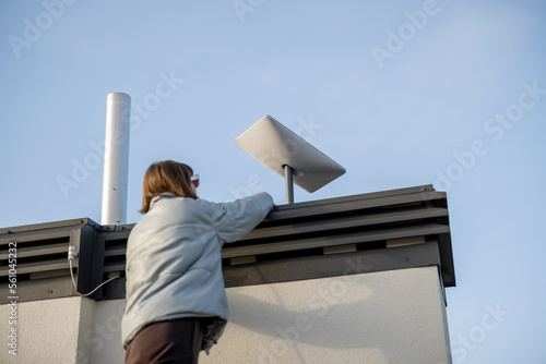 LVIV, UKRAINE - January, 2023: Woman installing Starlink satellite dish on roof of her house. Starlink is a satellite internet constellation operated by SpaceX