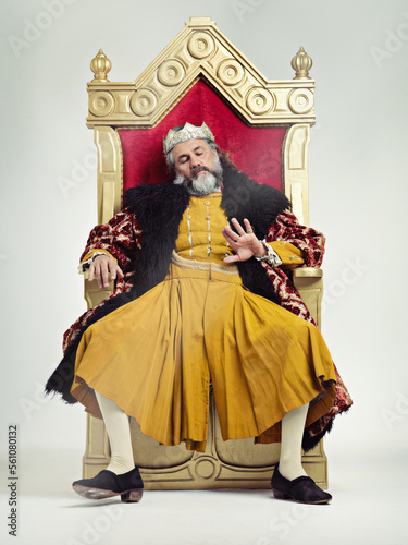 King, royalty and bored man on throne in studio isolated on gray background. Monarch, medieval royal and annoyed senior male, leader or frustrated ruler, looking at hand and sitting on golden seat.