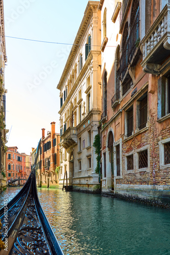 Gondola ride in Venice, Italy. View from gondola with narrow canal of water surrounded by old buildings on sunny spring day.