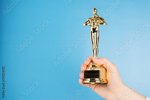 Oscar statue, award in hand on blue background,copy space