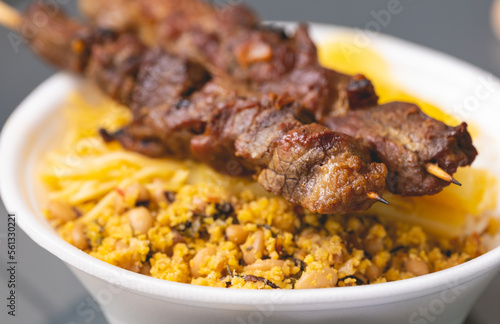 Churrasquinho brasileiro. Espetinhos com carne bovina sobre uma marmita de isopor com arroz, feijão tropeiro, mandioca cozida e macarrão. Comida brasileira, churrasco.