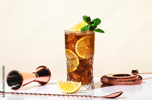 Long Island ice tea cocktail with vodka, rum, tequila, gin, liquor, lemon juice, cola and ice, garnished with lemon slice and mint in highball glass. Beige background, hard light
