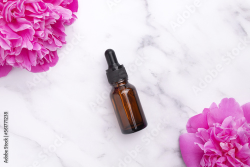 Glass dropper bottle on marble background with peony flower. Hyaluronic acid oil, serum with collagen and peptides skin care product. Mockup packaging, cosmetic design branding