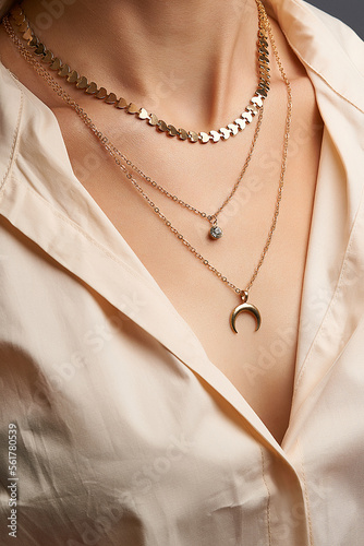 Cropped close-up portrait of a woman, demonstrating gold necklaces with pendants in a beige shirt. Set of three different chains. One necklace has a crescent moon pendant.