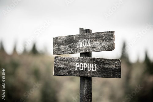 vintage and rustic wooden signpost with the weathered text quote vox populi, outdoors in nature. blurred out forest fall colors in the background.