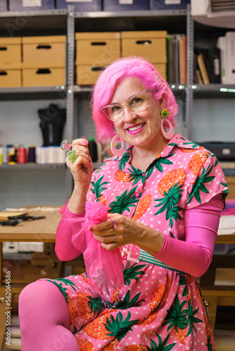 Dressmaker with pink hair and colorfull clothes hand sewing a piece of fabric.