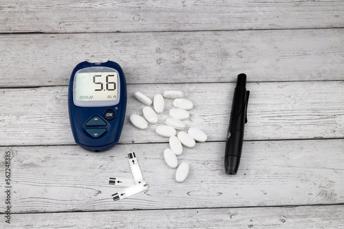 The glucose meter, auto lancet and pills on wooden background.
