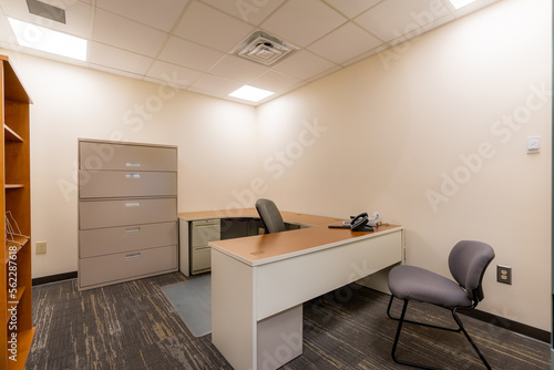 Depressing dull office with no window. Typical uninspiring empty office with desk, chair, file cabinet.