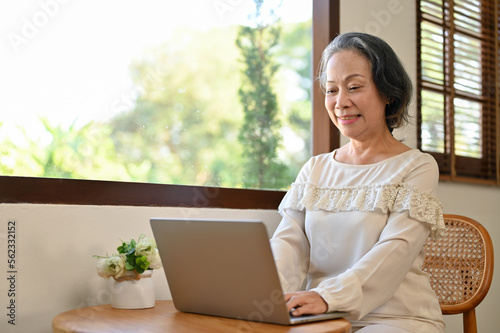 Charming aged Asian female entrepreneur remote working at home, using laptop computer.