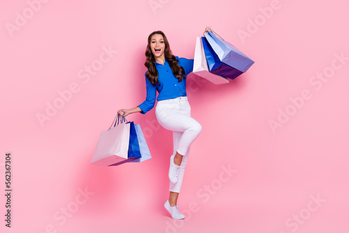 Full body length size photo of overjoyed shopaholic lady wear blue blouse fist up hold bags new cheap clothes isolated on pink color background