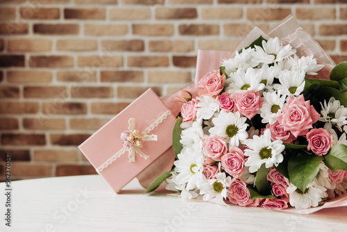 Beautiful bouquet of rose and chrysanthemums flowers and pink gift box on brick wall background. Gift for holiday, birthday, Wedding, Mother's Day, Valentine's day, Women's Day. Floral arrangement.