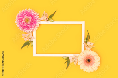 Frame made of green leaves, alstroemeria and gerbera flowers on a yellow background.