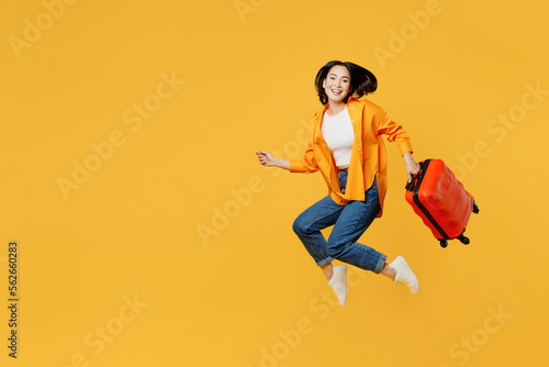 Side view fun young woman in summer casual clothes jump high hold suitcase isolated on plain yellow background. Tourist travel abroad in free spare time rest getaway. Air flight trip journey concept