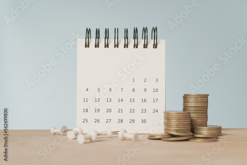 For payday loan concept. White calendar and blurred stack of coins , blurred white thumbtack on wood desk