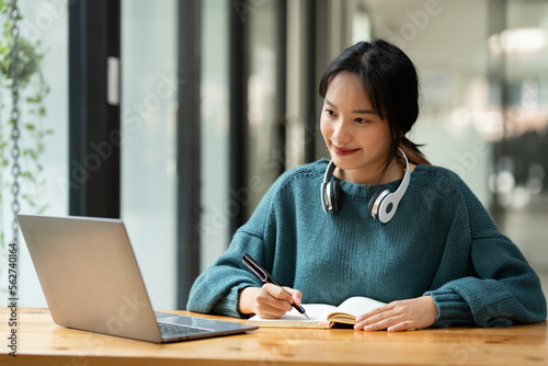 Portrait of Asian businesswoman sitting happily working on laptop and taking notes fluently and smiling happily with her assignments. management concept.