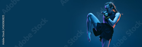 Leg kick. Young woman athletic female MMA fighter training isolated on gradient blue-pink background in neon light. Concept of sport, competition, action